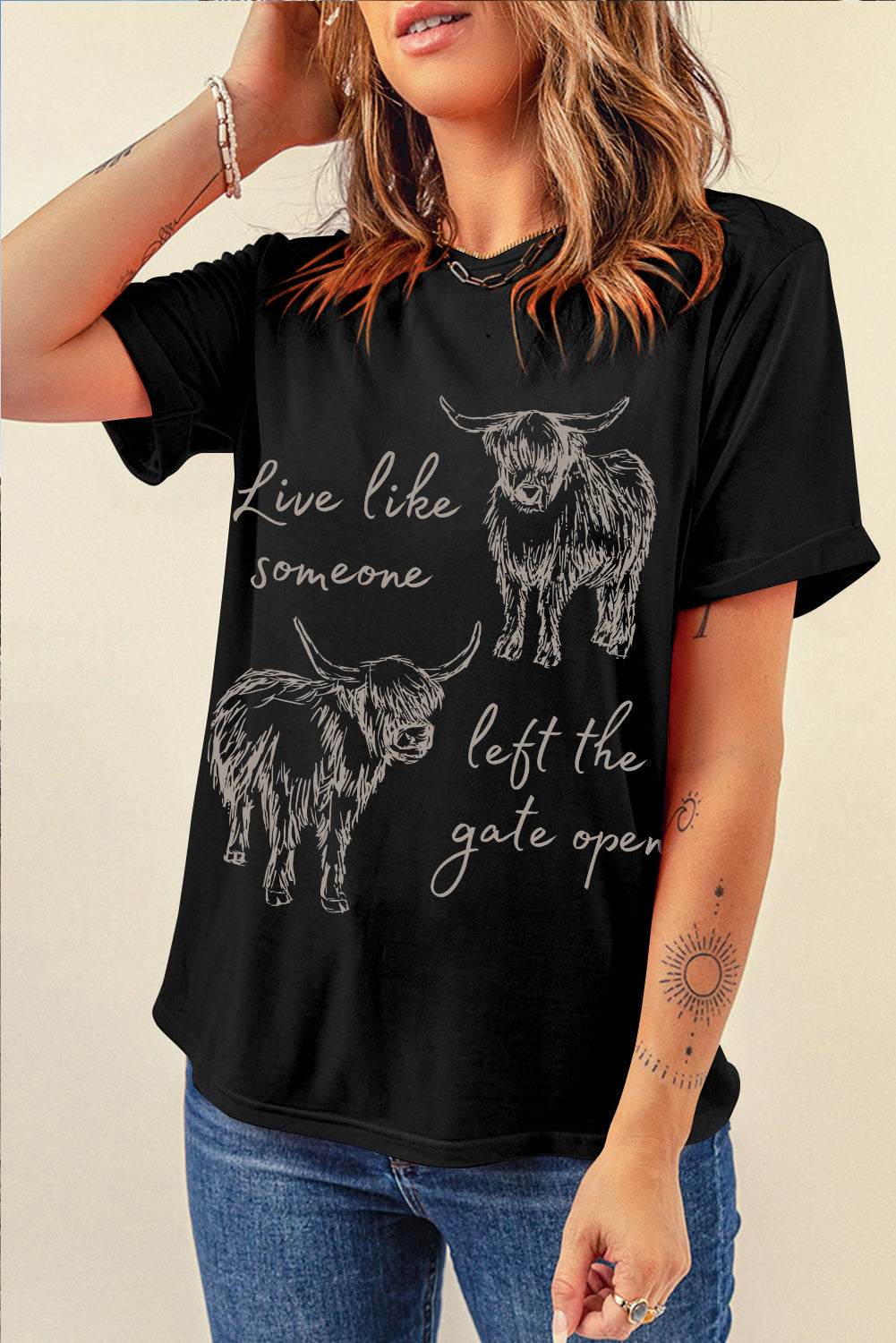 Black Western Cow Print Graphic Tee featuring white highland cow illustrations and cursive text on a classic crew neck black fabric.