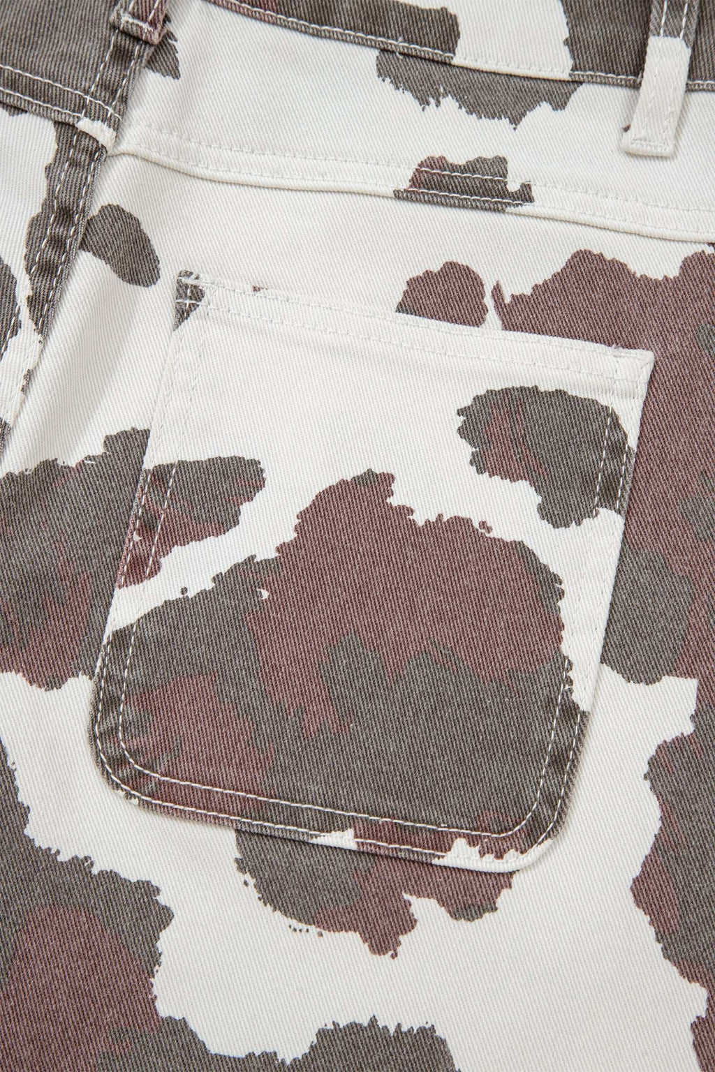 Jeans fabric with Brown Cow Print pattern in brown and white featuring a stitched back pocket and cotton blend material.